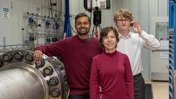 two men and a woman stand inside a scientific laboratory